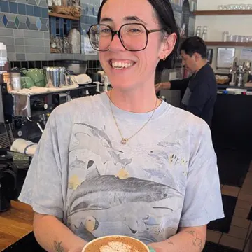 A Beans barista holding up the latte she made