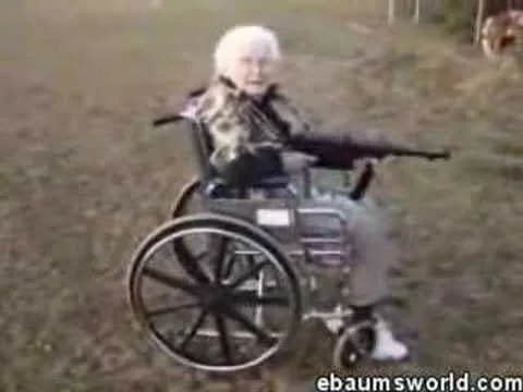 An elderly woman in a wheelchair outdoors, holding a rifle in shooting position