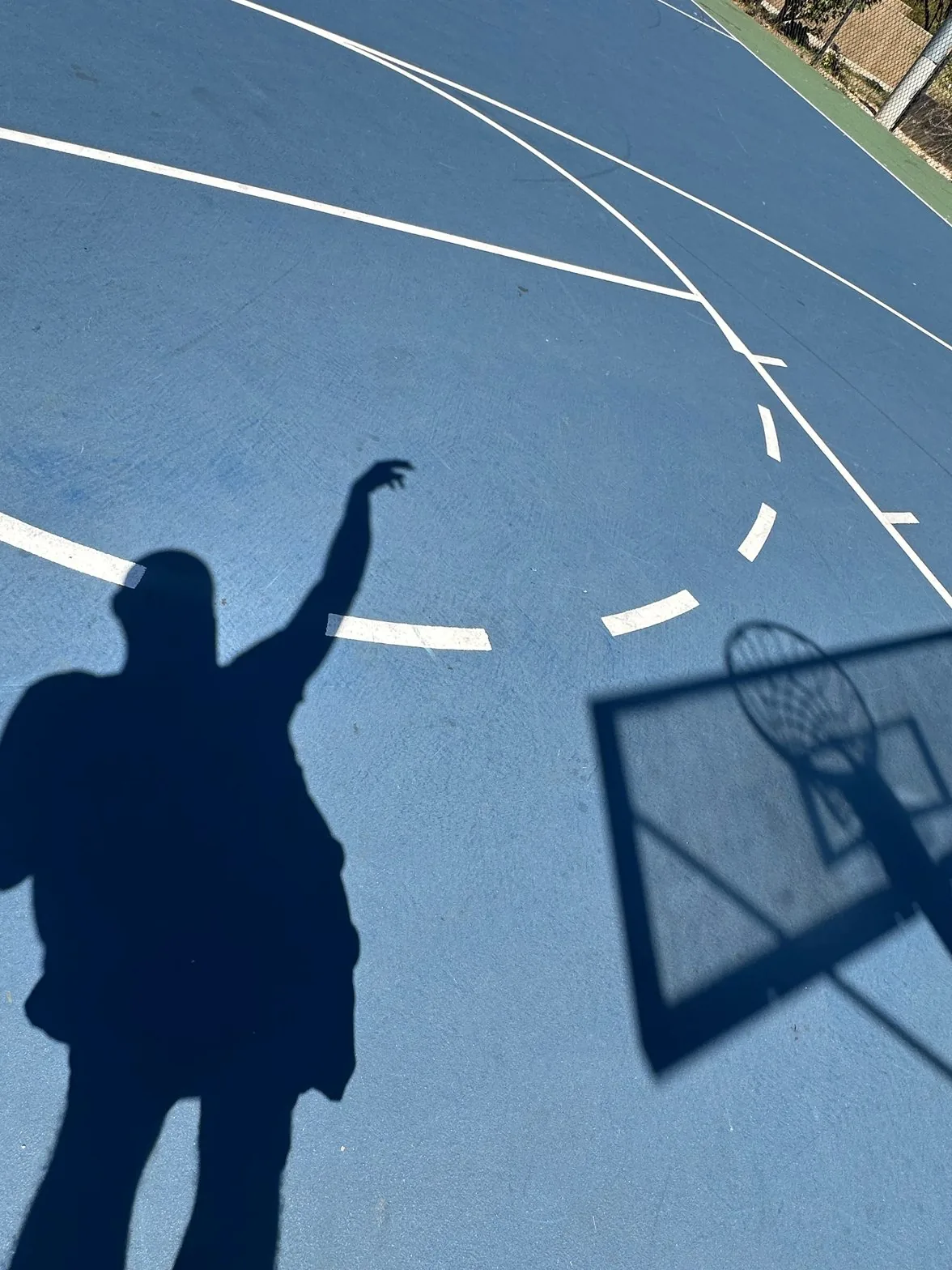 Shadow of person with raised arm on blue basketball court